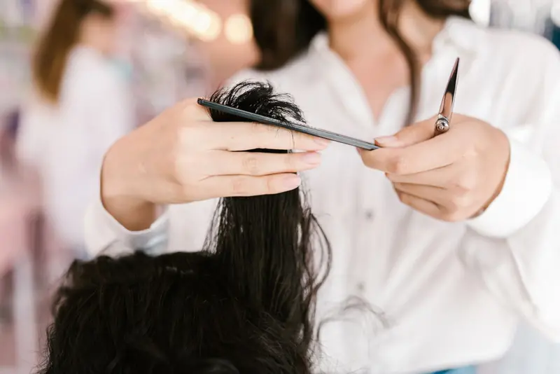 Estilista cortando un mechón de pelo oscuro con tijera y peine.