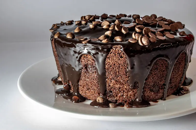 Torta de chocolate cubierta con ganache y chips de chocolate, sobre un plato blanco.