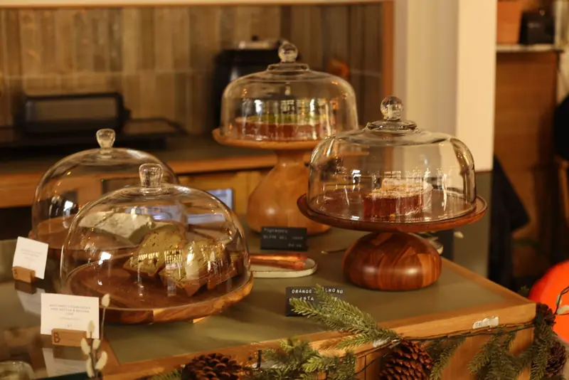 Tortas caseras bajo campanas de vidrio sobre una mesa de madera.