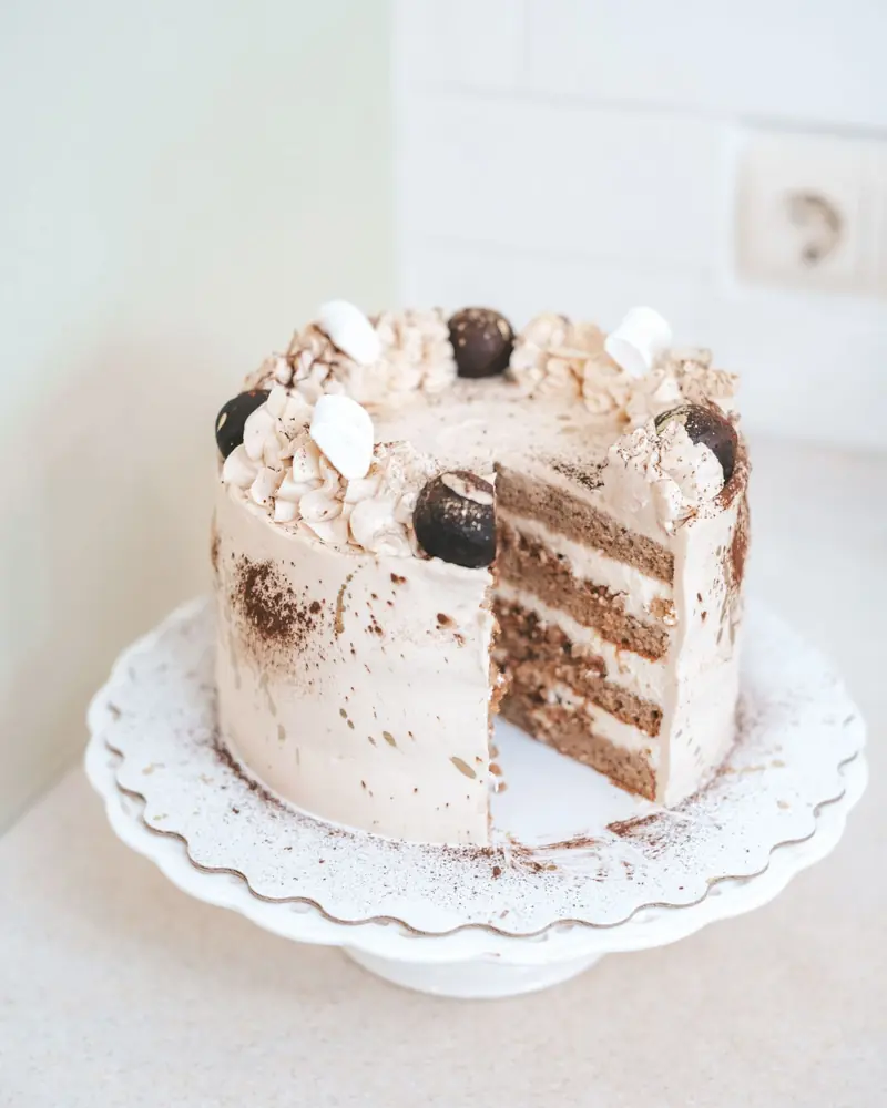 Torta de varias capas cubierta de crema clara, con un corte que muestra el relleno.